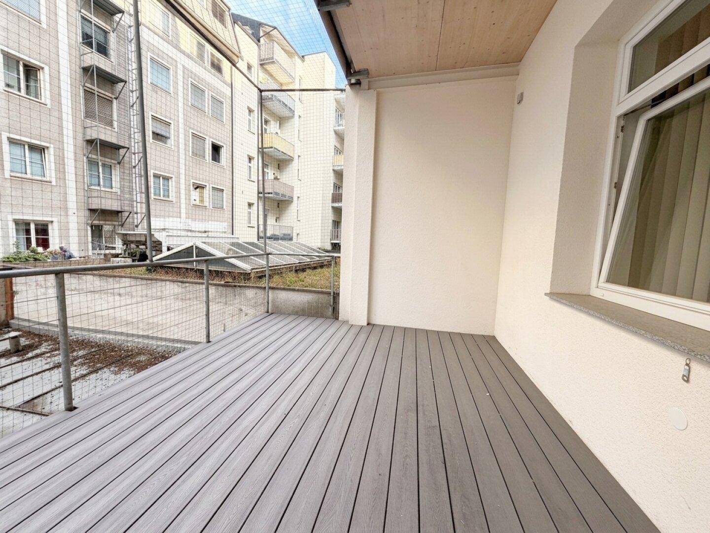 Geräumiger Balkon mit modernen grauen Dielen und Blick auf den Innenhof.
