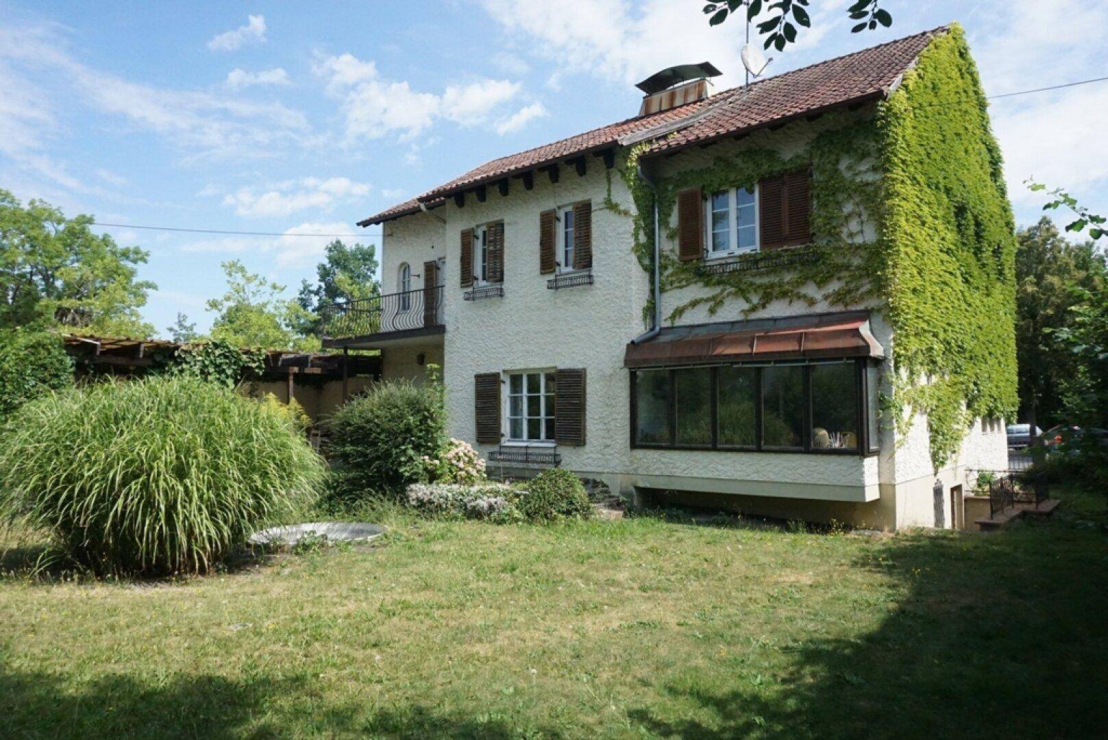 Seitliche Ansicht des Hauses mit üppigem Efeu, Garten und Wintergarten.