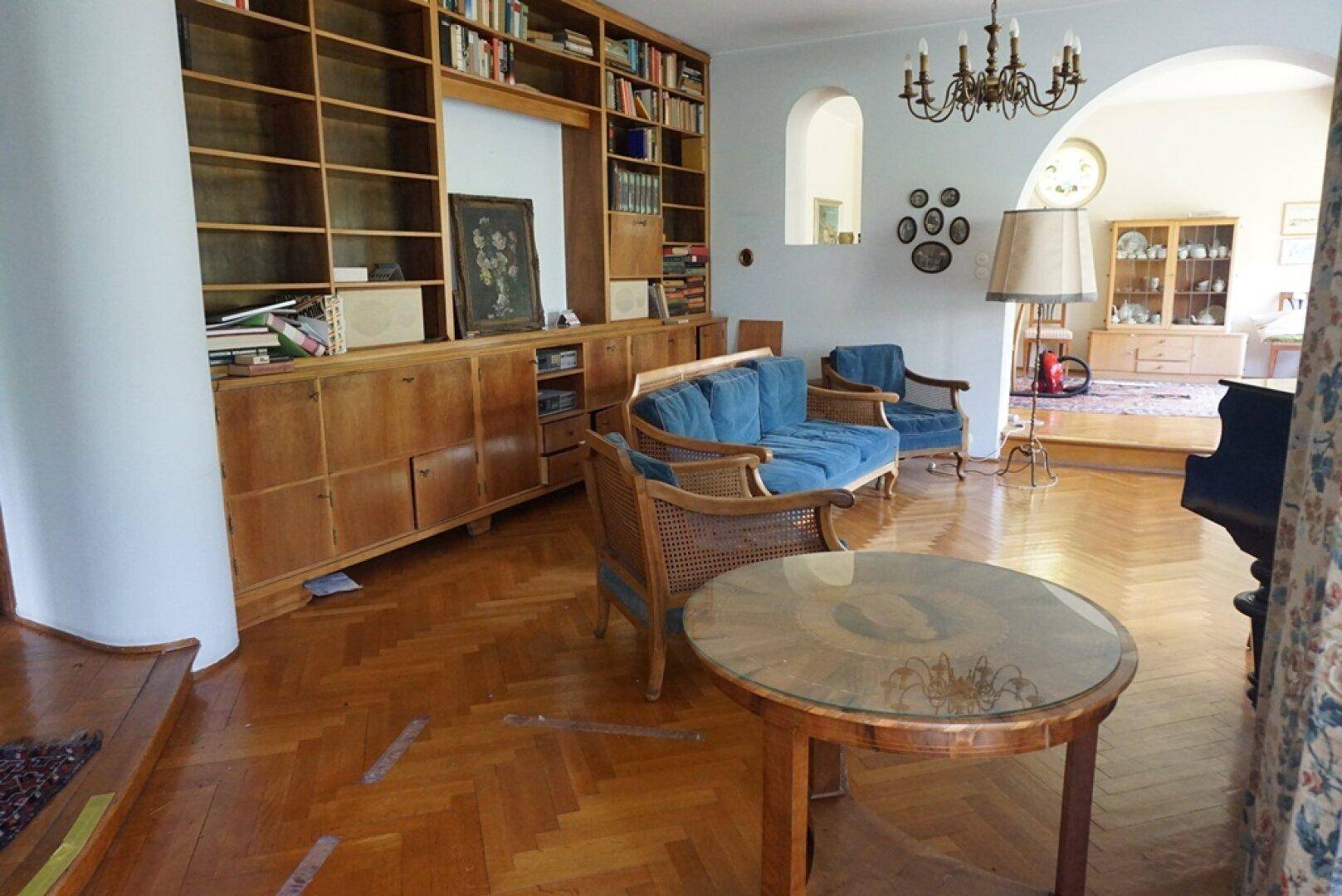 Geräumiges Wohnzimmer mit Fischgrätparkett, eingebauten Holzregalen und blauen Sofas.