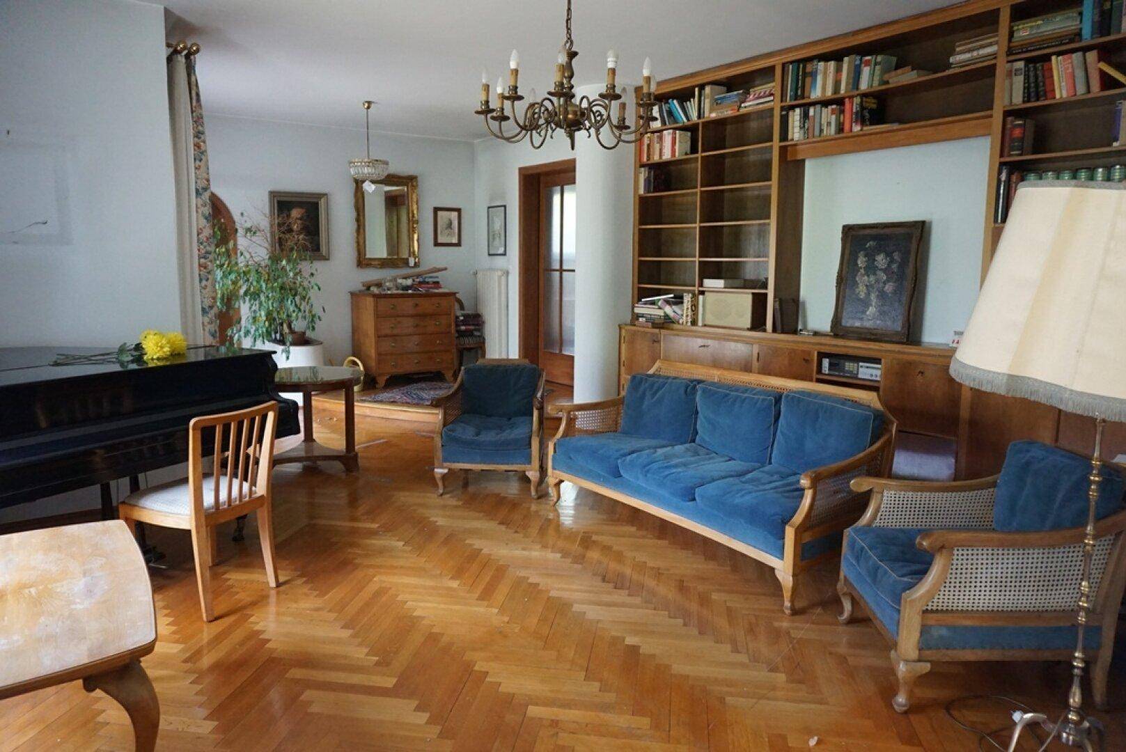 Helles Wohnzimmer mit Klavier, Parkettboden und umfangreicher Bücherwand.