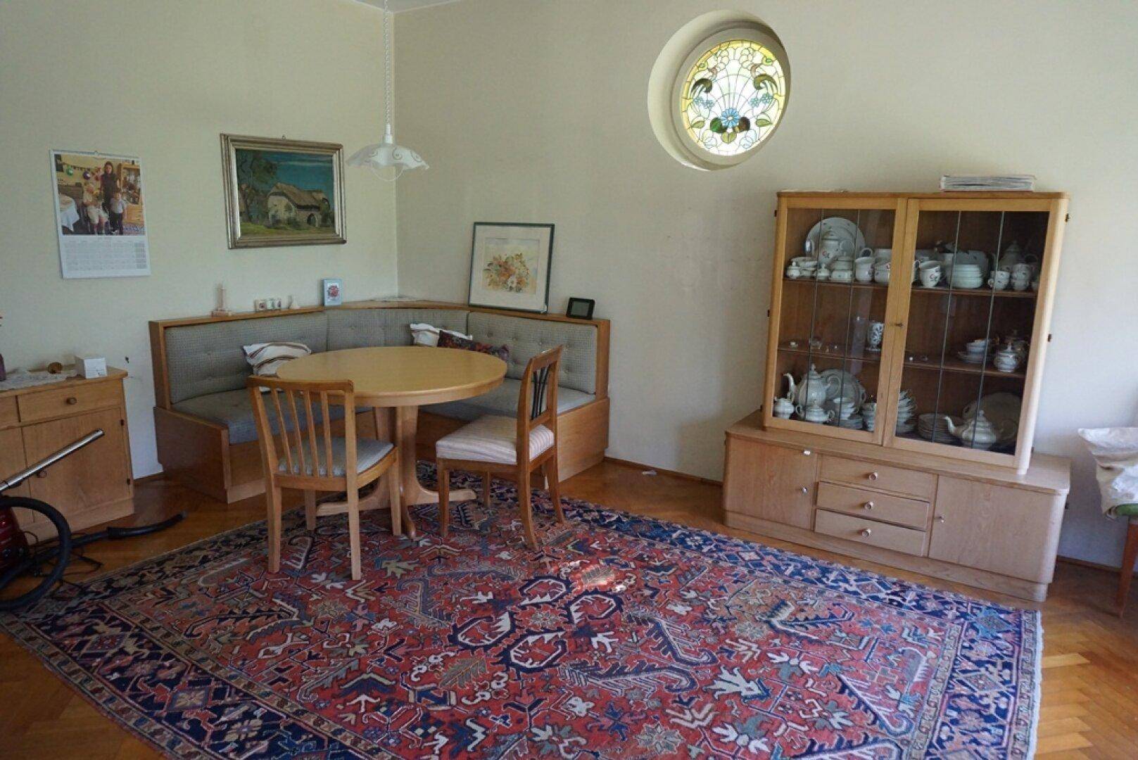 Gemütlicher Essbereich mit Eckbank, Holztisch und dekorativem Buntglasfenster.