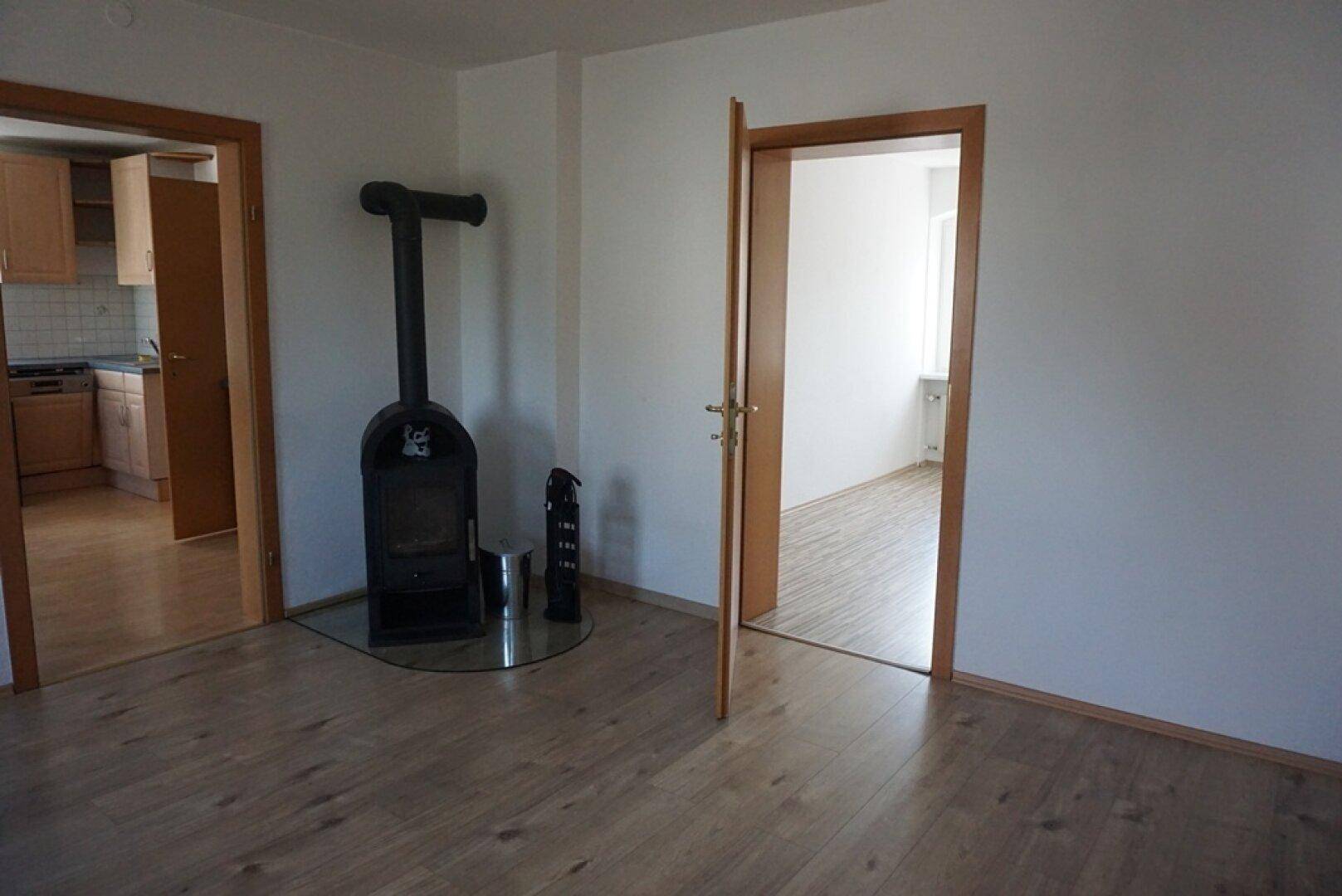 Helles Wohnzimmer mit Laminatboden und einem gemütlichen Holzofen als zusätzliche Wärmequelle.