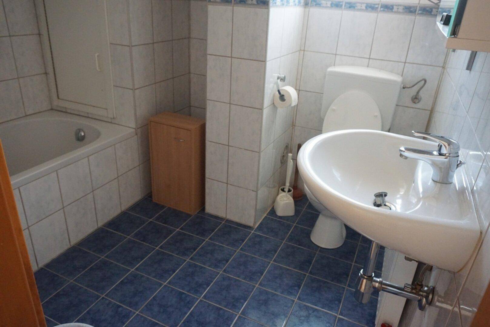 Badezimmer mit blauen Bodenfliesen, weiß gefliesten Wänden, einer Badewanne und einem Waschbecken.