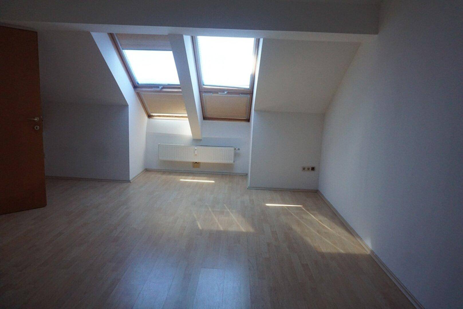Helles Dachgeschosszimmer mit schrägen Wänden, Laminatboden und zwei großen Dachfenstern.