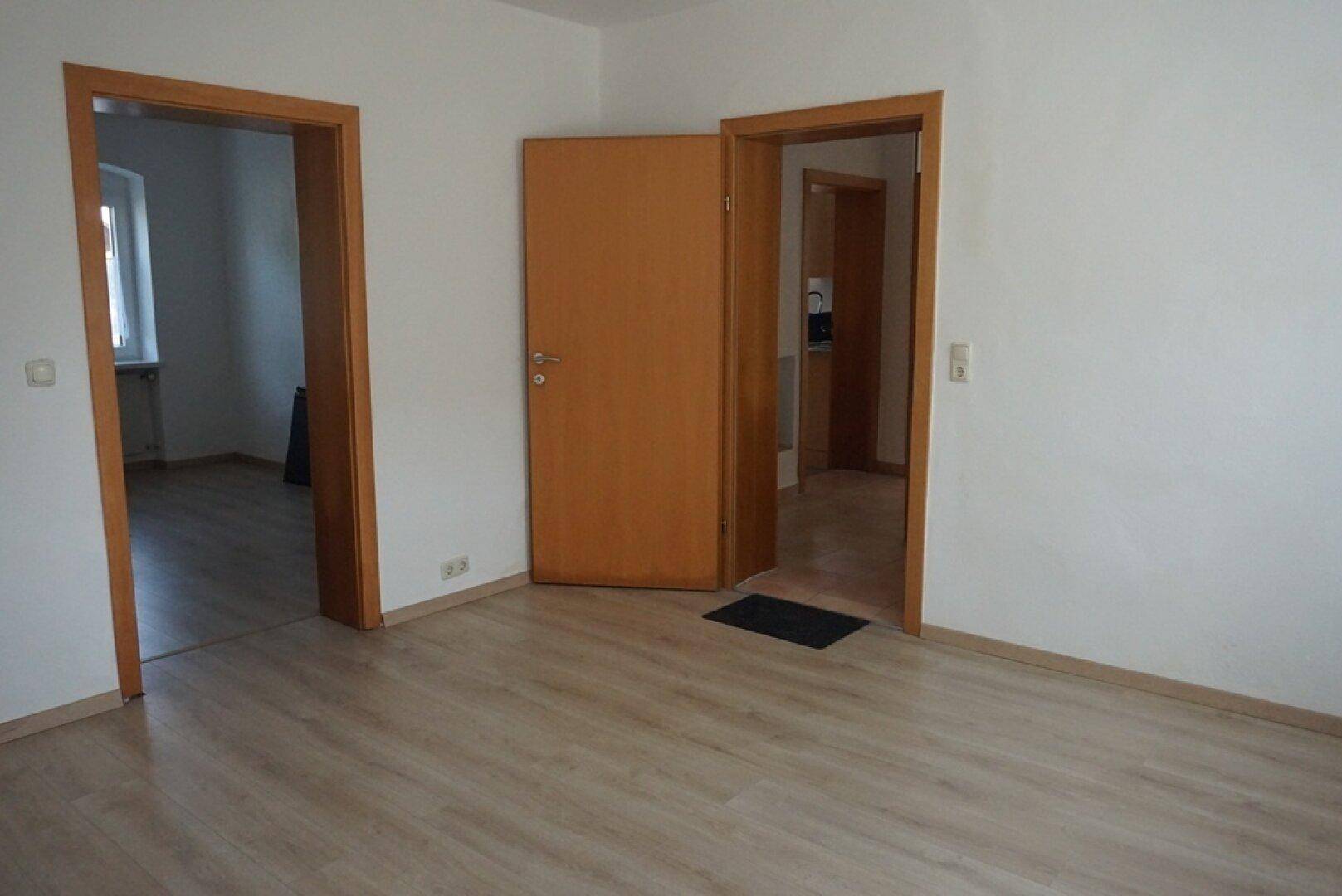 Geräumiger Wohnbereich mit Laminatboden und offenen Türen, die zu weiteren Zimmern führen.