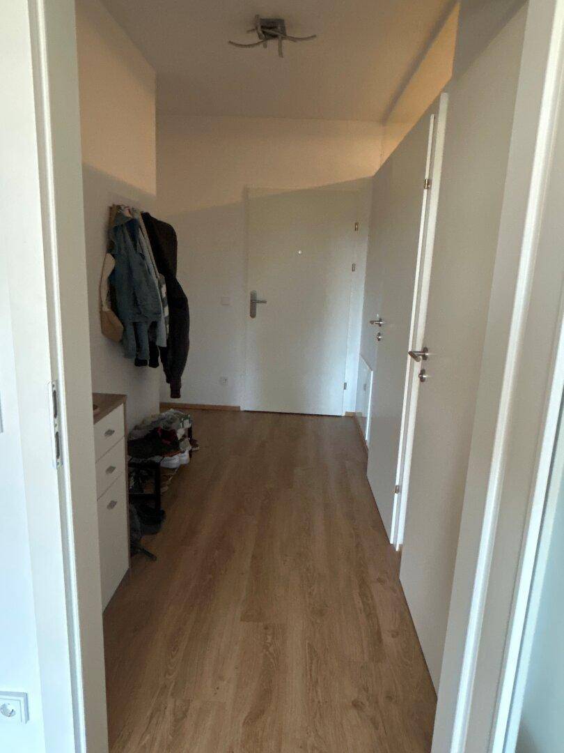 Heller Flur mit Laminatboden und weißen Wänden, der zu weiteren Räumen führt.