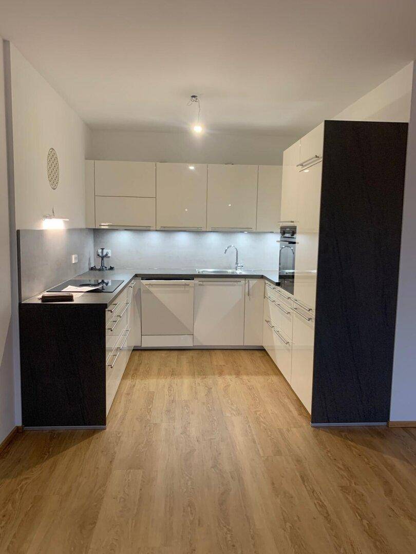 Moderne U-förmige Küche mit weißen Hochglanzfronten, dunkler Arbeitsplatte und integrierten Geräten.