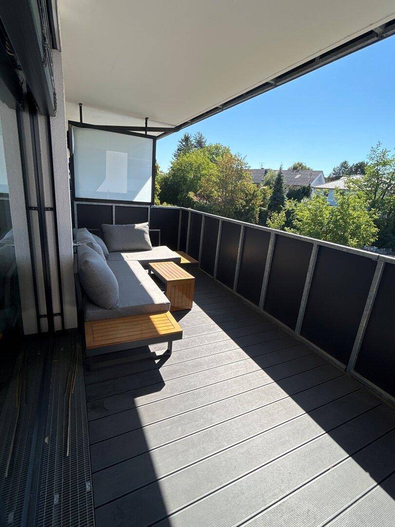 Sonniger Balkon mit bequemer Outdoor-Sitzgruppe und Blick ins Grüne.