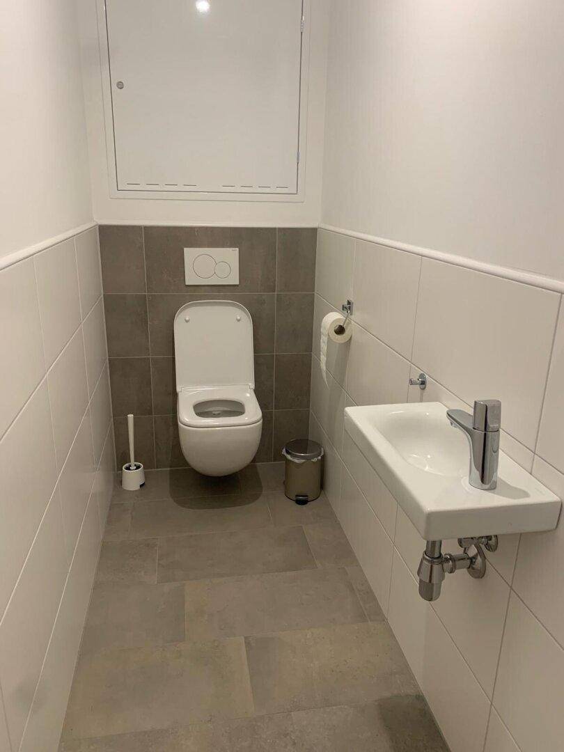 Modernes Gäste-WC mit wandhängendem WC, kleinem Waschbecken und hellen Fliesen.
