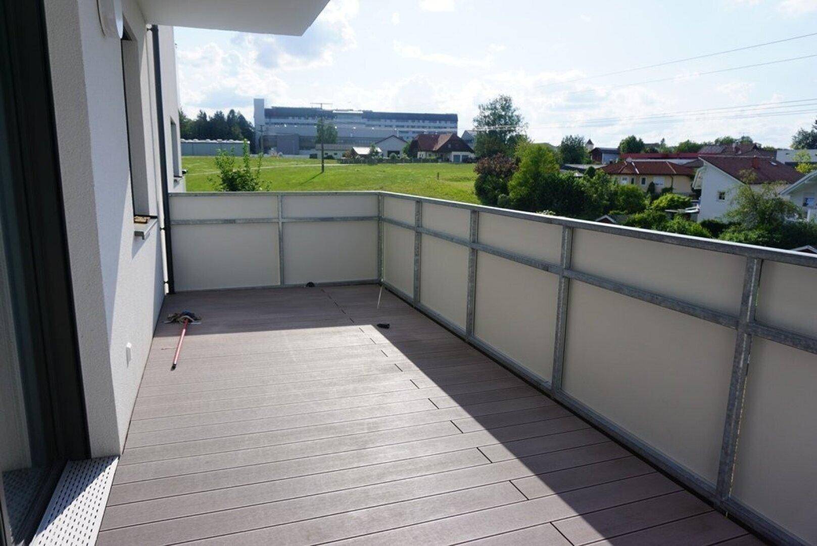 Geräumiger Balkon mit Holzdielenboden und Blick auf die Umgebung unter sonnigem Himmel.
