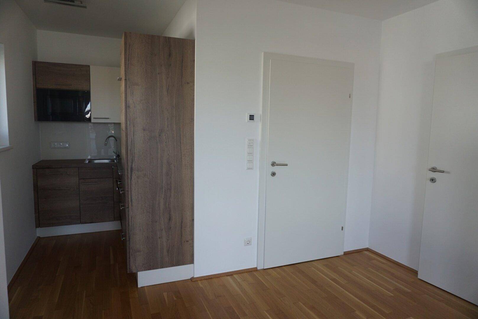 Kleine, moderne Küchenzeile mit Holzelementen und integrierten Geräten in einem hellen Raum.