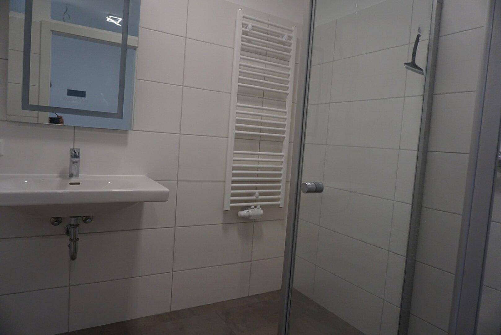 Modernes Badezimmer mit weißen Fliesen, Duschkabine und beheiztem Handtuchhalter.