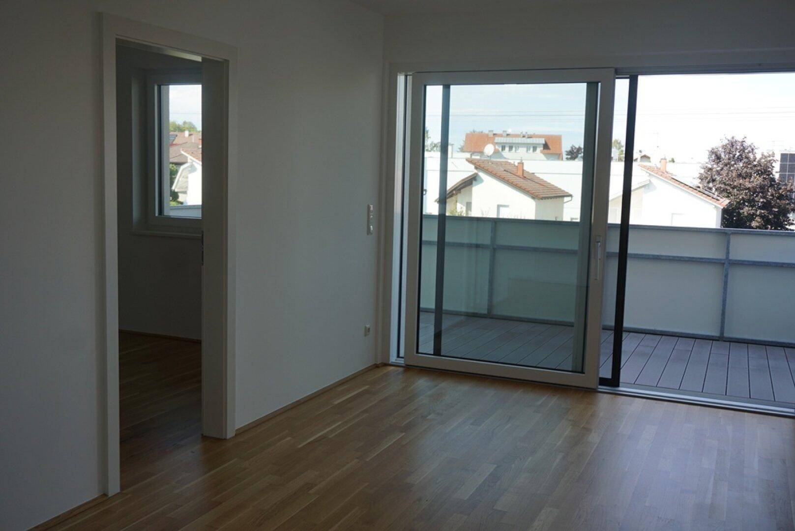Heller Wohnraum mit Holzboden und großem Schiebefenster zum Balkon, bietet weite Aussicht.