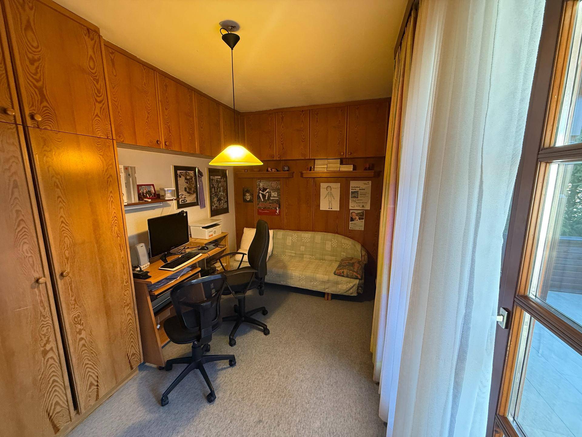 Helles Arbeitszimmer mit Einbauschränken, Schreibtisch und Zugang zu einem Außenbereich.