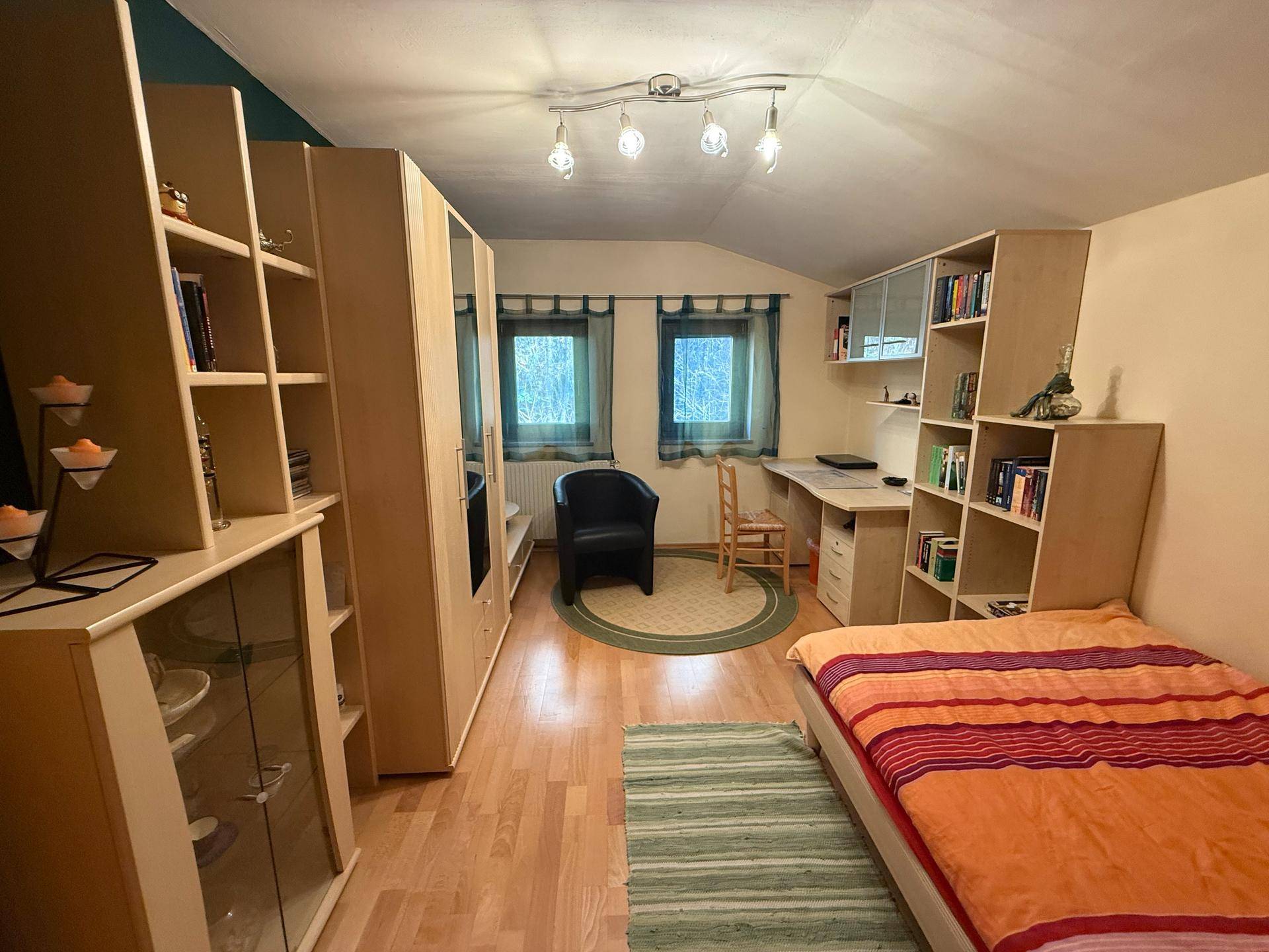 Helles Schlafzimmer mit Dachschräge, Holzfußboden und praktischen Regalsystemen.