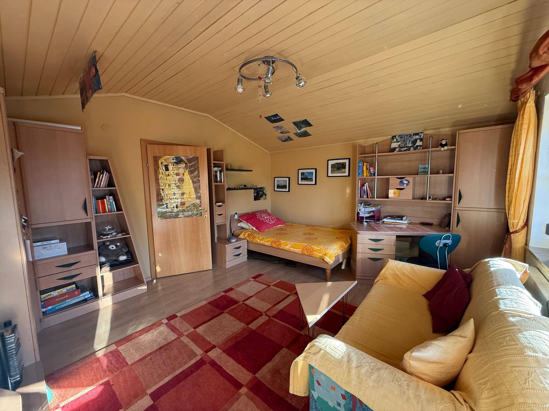 Gemütliches Schlafzimmer mit Dachschräge, Holzboden und farbenfroher Dekoration.