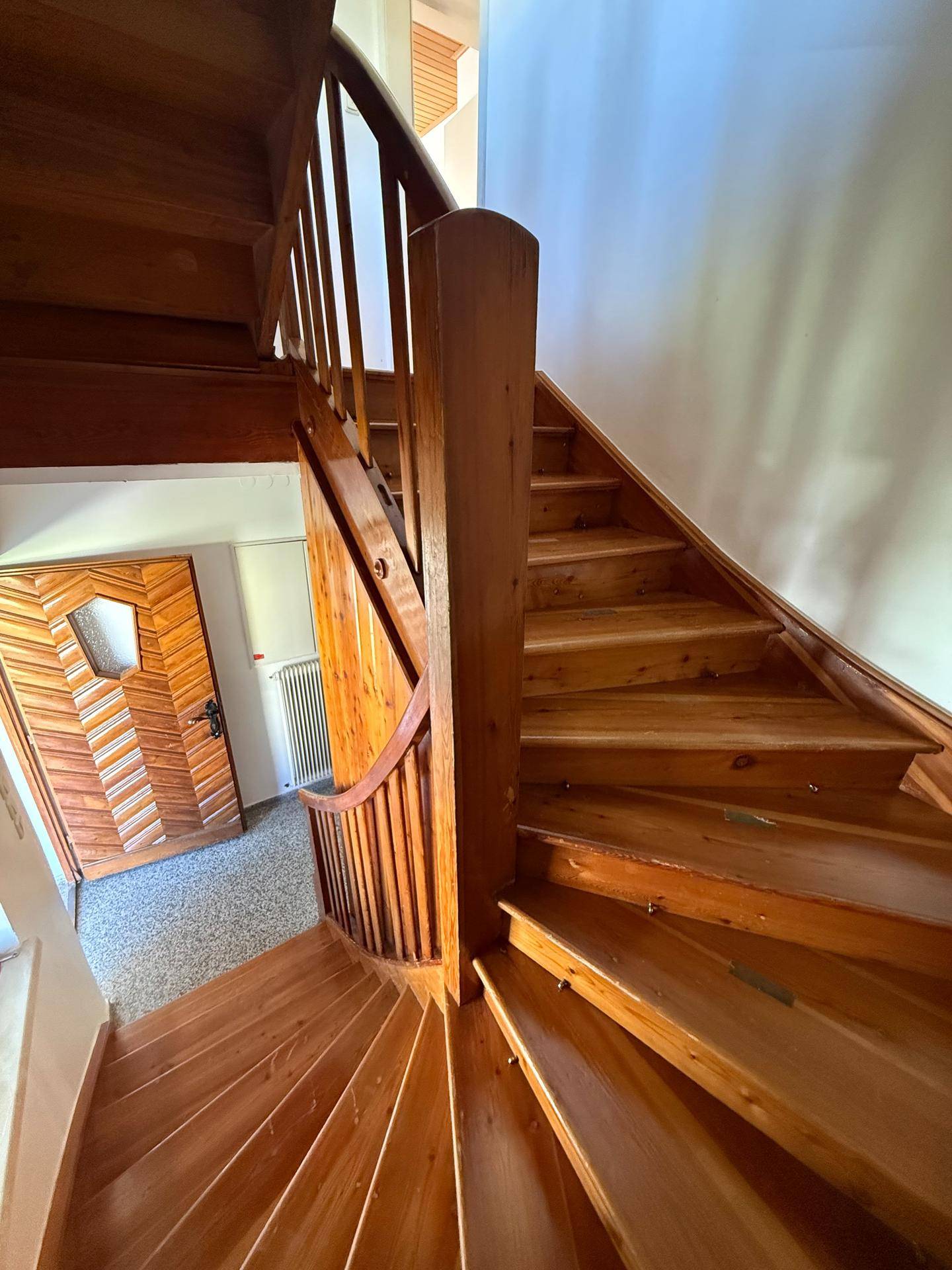 Warme Holztreppe mit Geländer und einer dekorativen Holztür im Eingangsbereich.