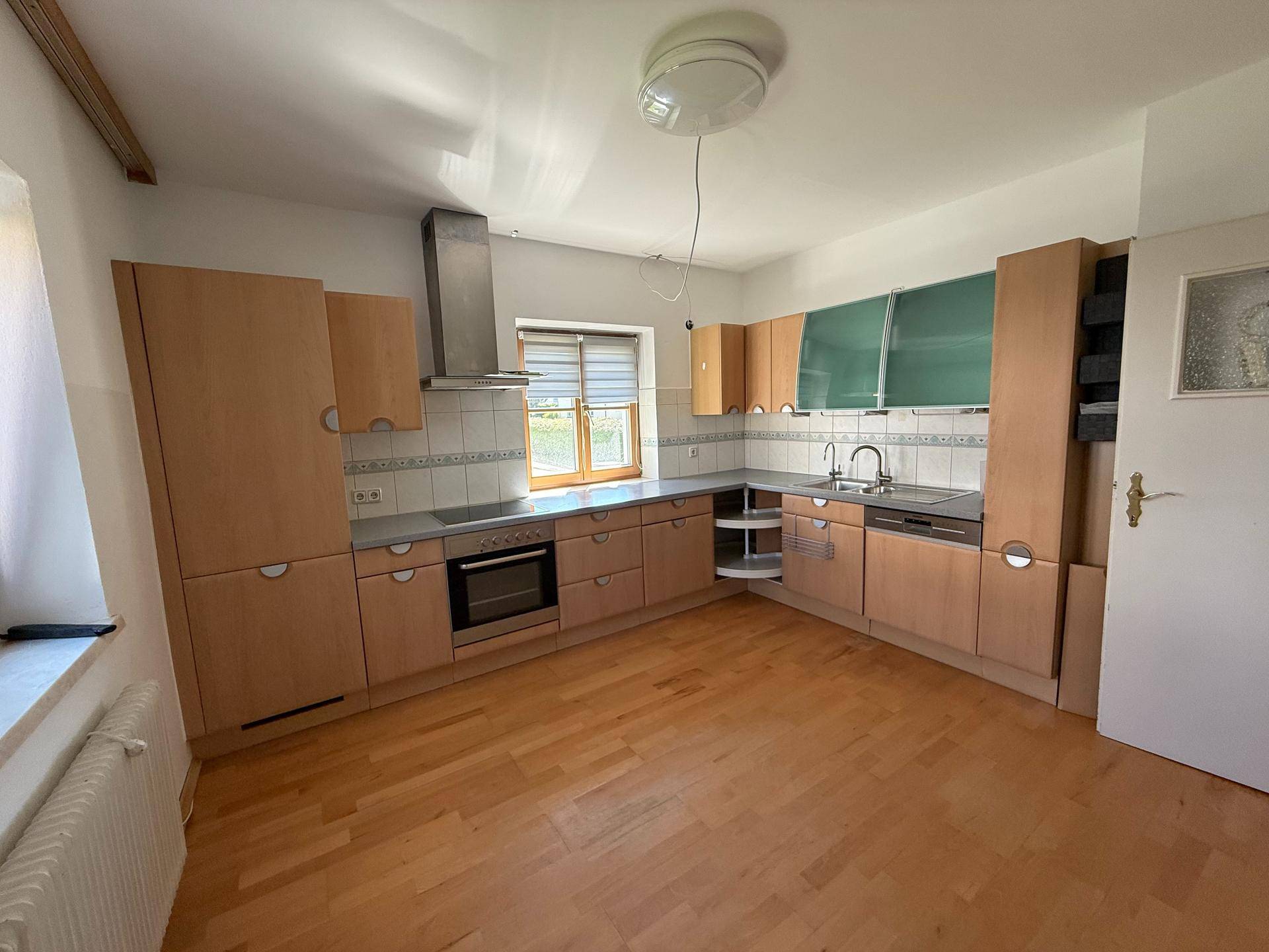 Funktionale Küche mit hellen Holzschränken, dunklen Arbeitsplatten und Parkettboden.