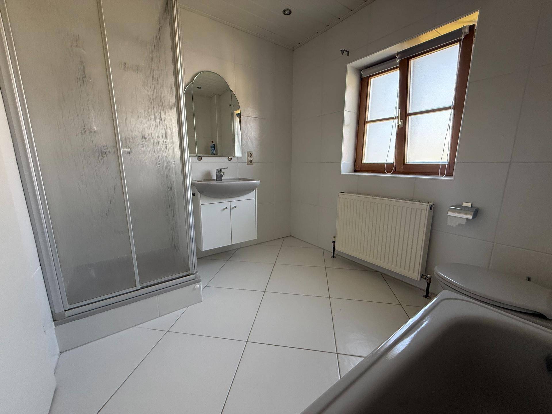 Helles Badezimmer mit weißen Fliesen, Duschkabine, Badewanne und Fenster für Tageslicht.