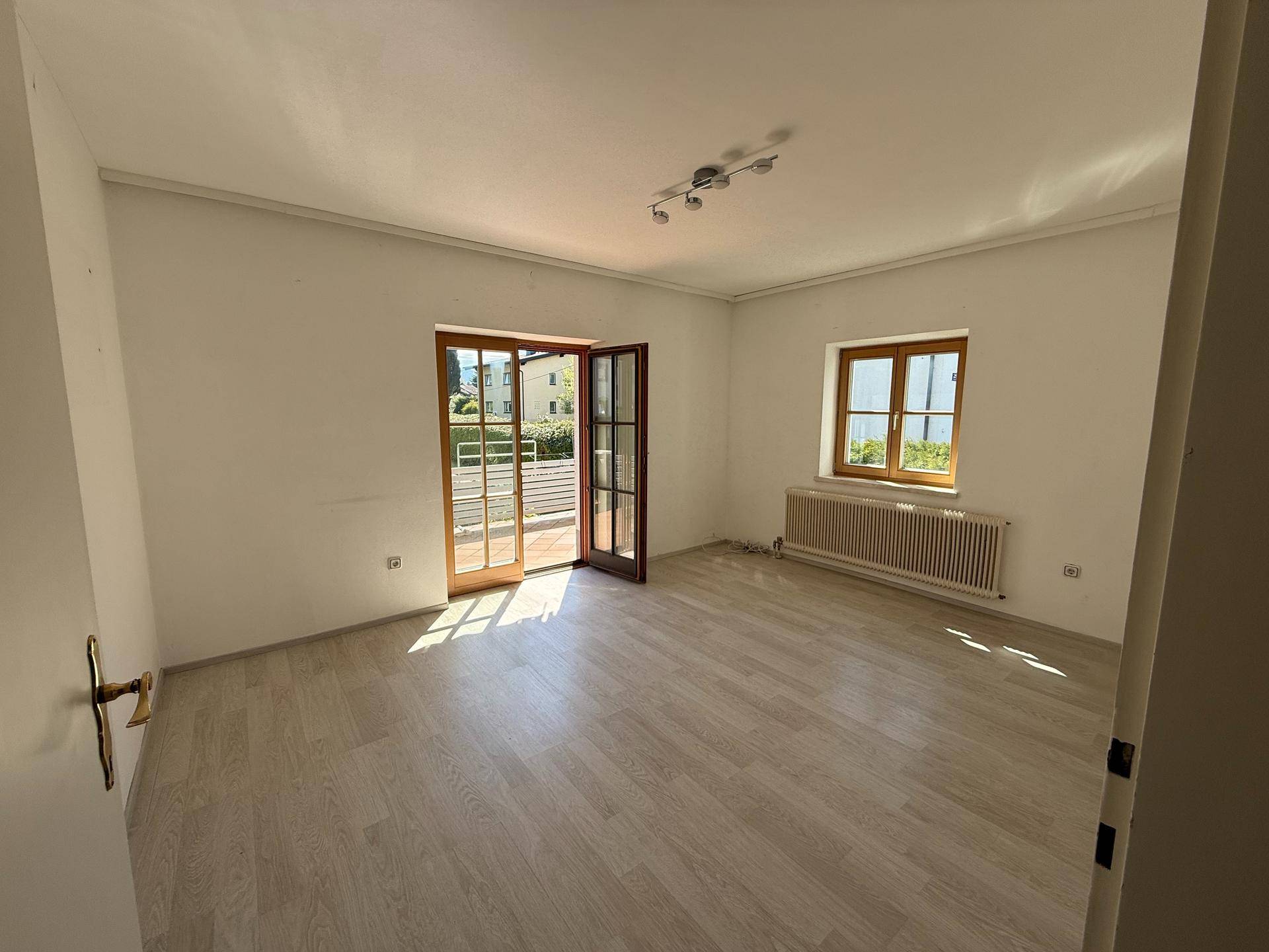 Helles Zimmer mit hellem Laminatboden, weiß gestrichenen Wänden und Zugang zu einem Balkon.