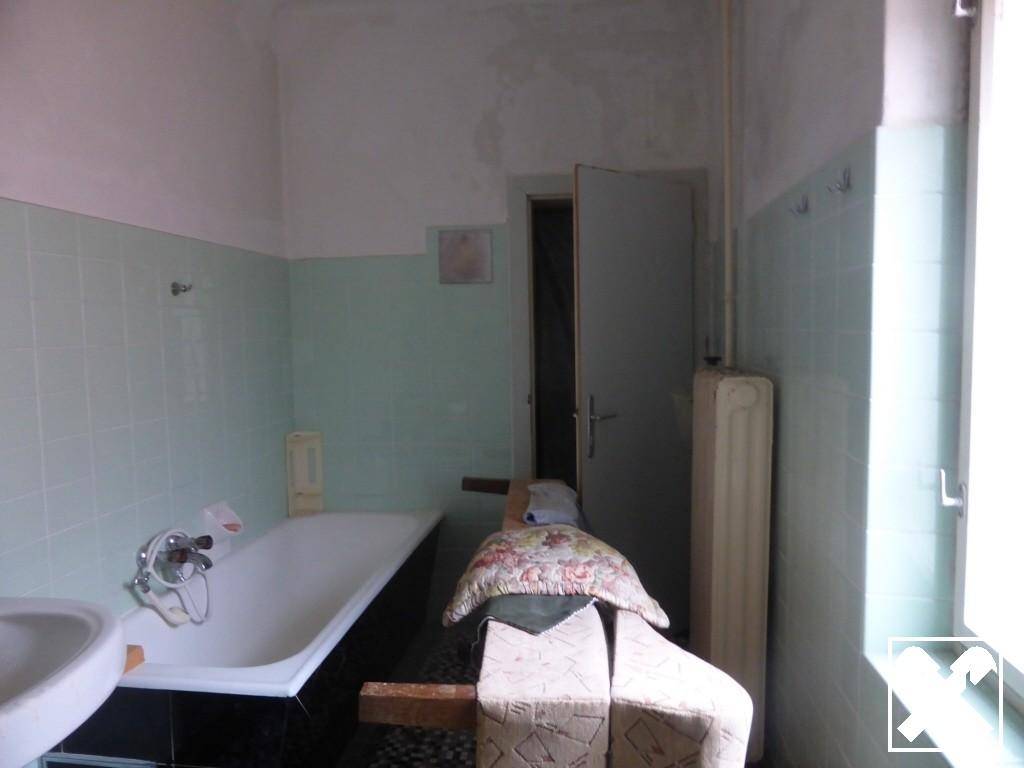 Badezimmer mit Badewanne, Waschbecken und hellgrünen Fliesen, das eine Renovierung benötigt.