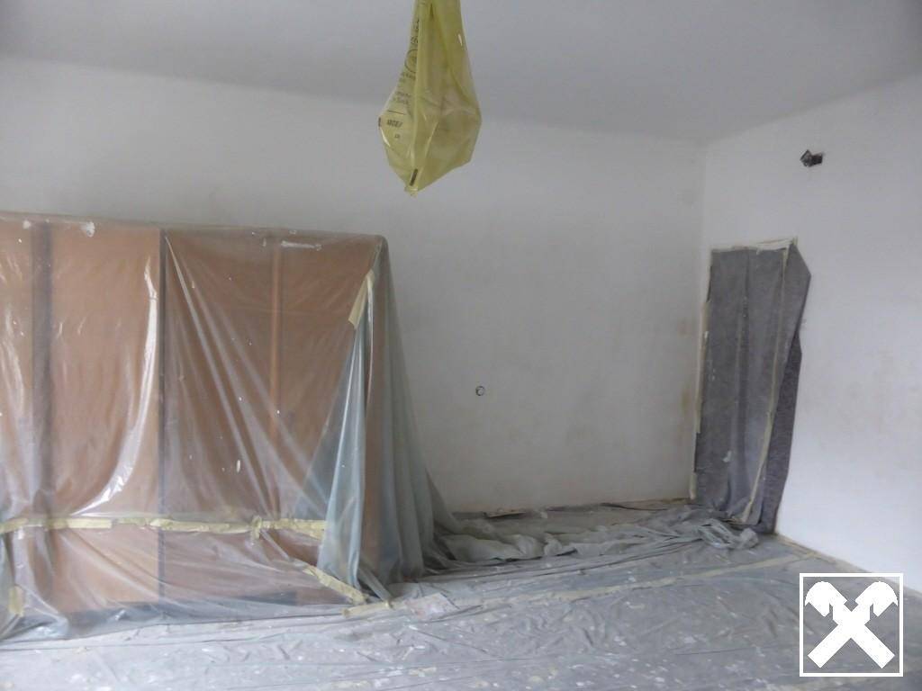 Innenraum, der für Renovierungsarbeiten vorbereitet ist, mit abgedeckten Möbeln und Böden.