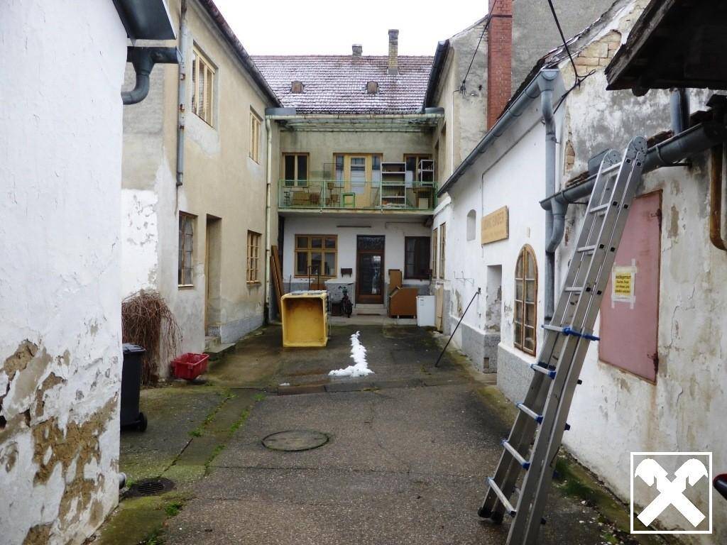 Innenhof zwischen Gebäuden mit Leiter und verschiedenen Gegenständen, der eine Renovierung benötigt.