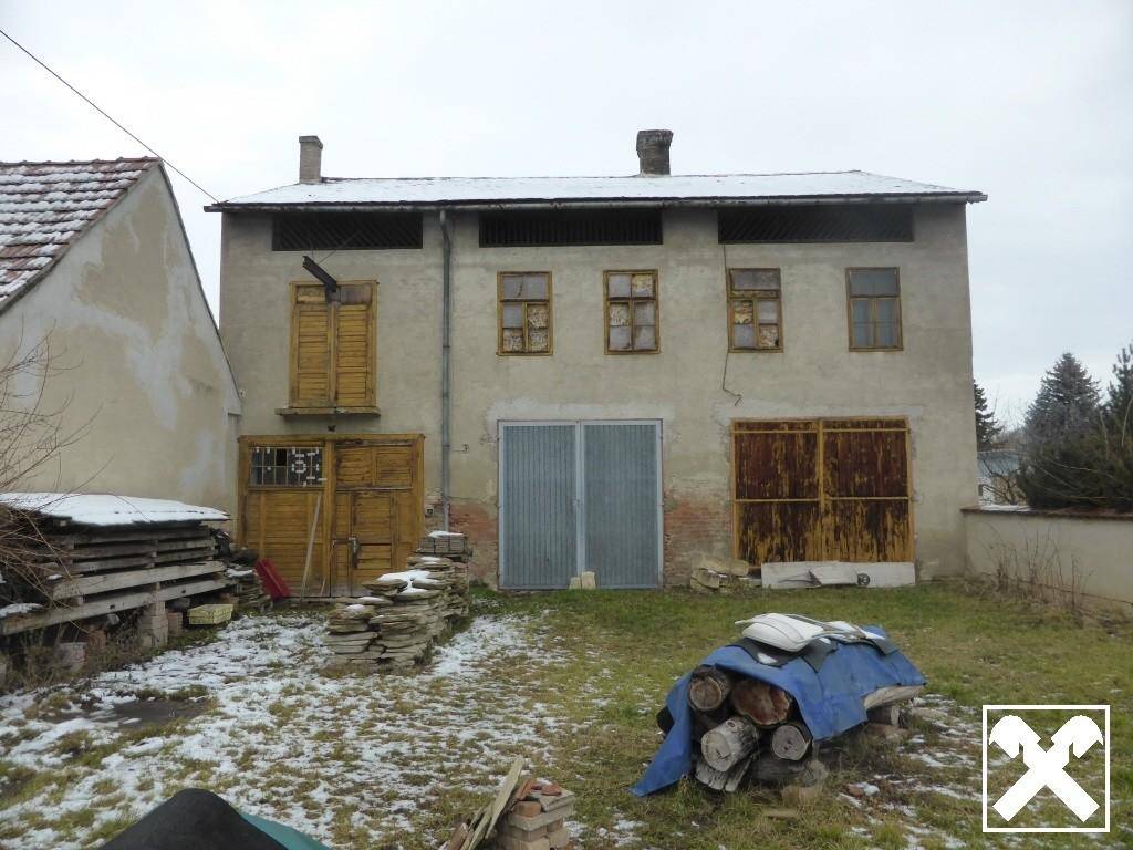 Rückseite eines alten Gebäudes mit Garten, Schnee und gestapeltem Holz, das eine Renovierung benötigt.
