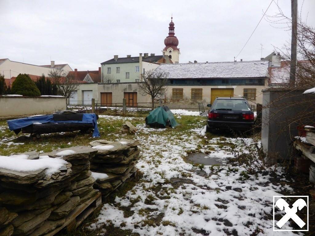Gartenbereich mit Schnee, einem geparkten Auto und einem Kirchturm im Hintergrund.