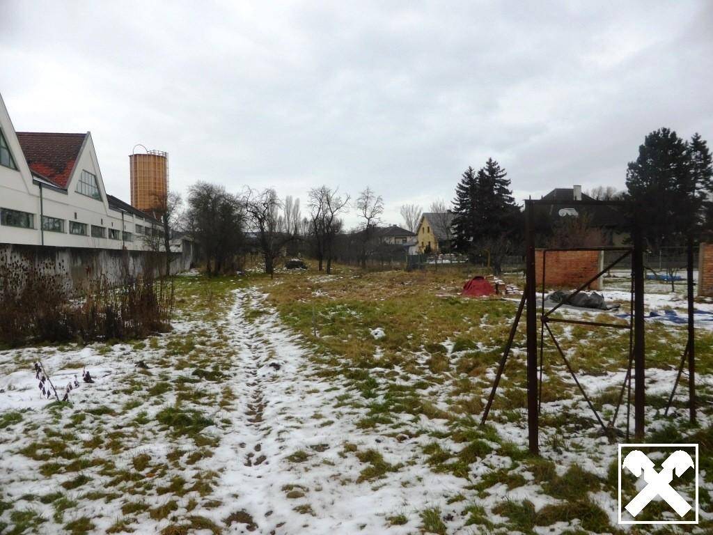 Weitläufiges Grundstück mit Gras und Schnee, umgeben von Bäumen und anderen Gebäuden in der Ferne.