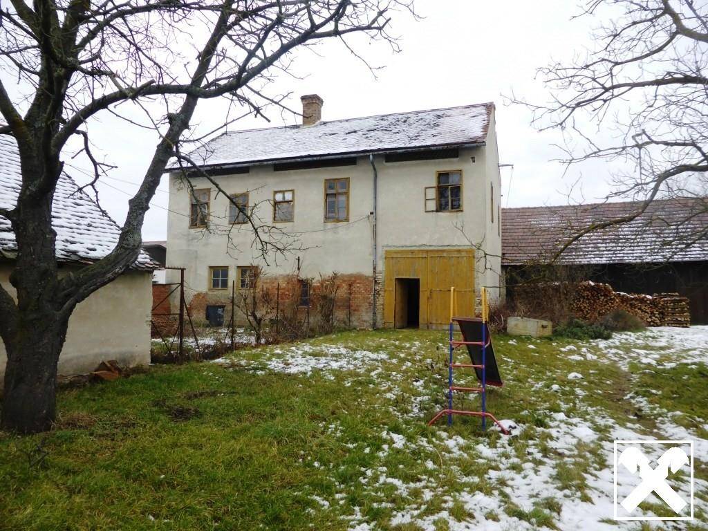 Hinteransicht eines alten Gebäudes mit Gartenbereich, Bäumen und einem kleinen Spielgerät im Schnee.
