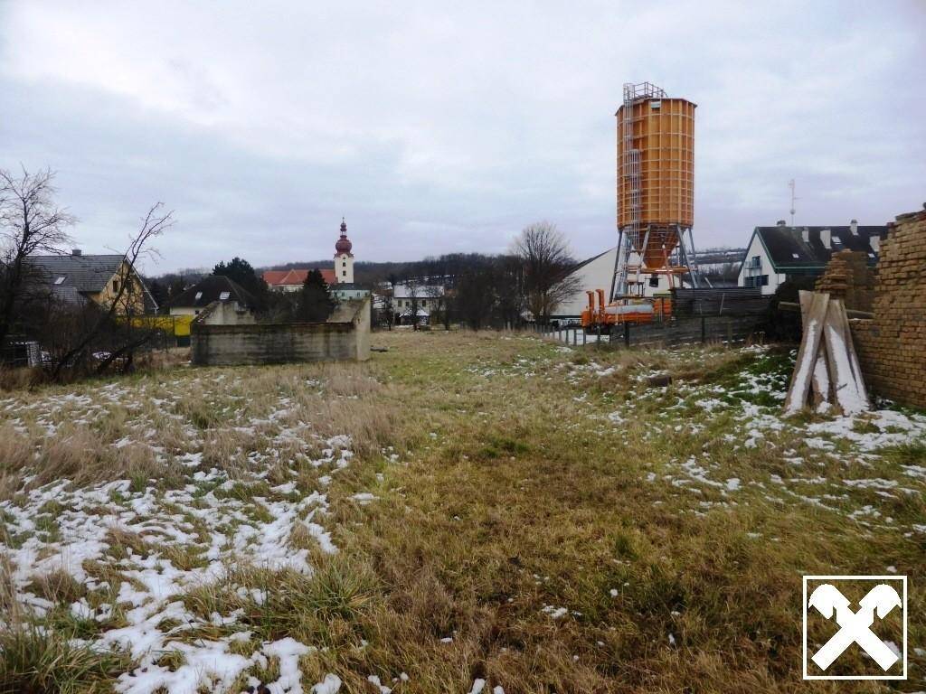 Weitläufiges, unbebautes Grundstück mit Gras und Schnee, im Hintergrund ein Wasserturm und Kirchturm.