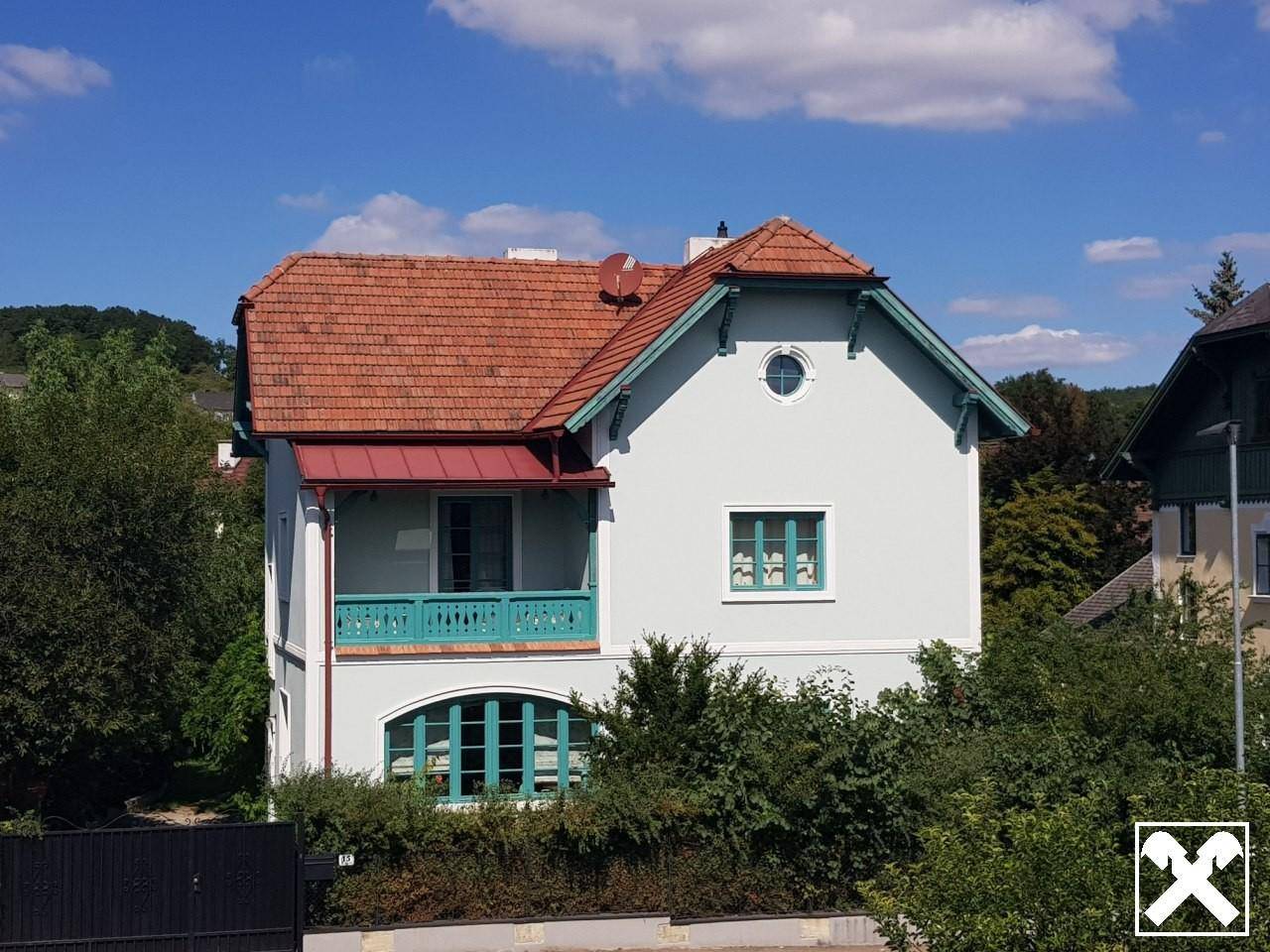 Detailansicht der Villa mit markantem Ziegeldach, Balkon und hellgrünen Fensterrahmen.