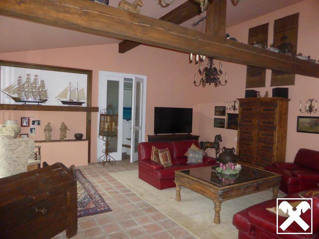 Geräumiges Wohnzimmer mit Holzbalken, roten Ledersofas und rustikalem Interieur.