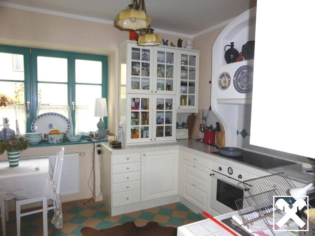 Traditionelle Küche mit weißen Schränken, kariertem Fliesenboden und Blick ins Grüne.