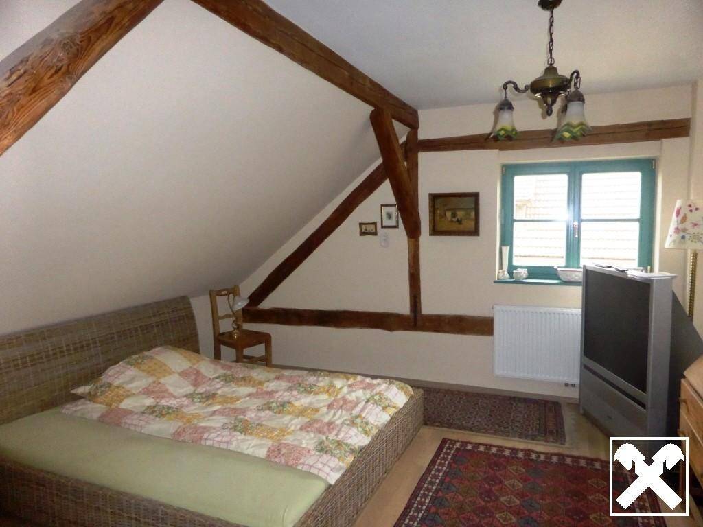 Gemütliches Schlafzimmer im Dachgeschoss mit sichtbaren Holzbalken und schrägen Wänden.