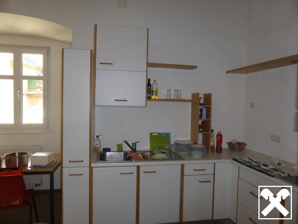 Funktionale Küche mit weißen Schränken, Spüle und einem Fenster, das Tageslicht hereinlässt.