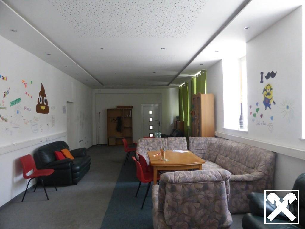 Heller Gemeinschaftsraum mit verschiedenen Sitzbereichen und großen Fenstern für viel Tageslicht.