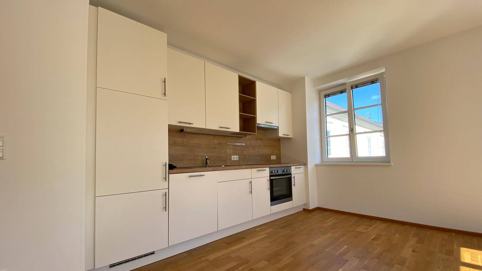 Helle, moderne Einbauküche mit weißen Schränken, Holzakzenten und Fensterblick.