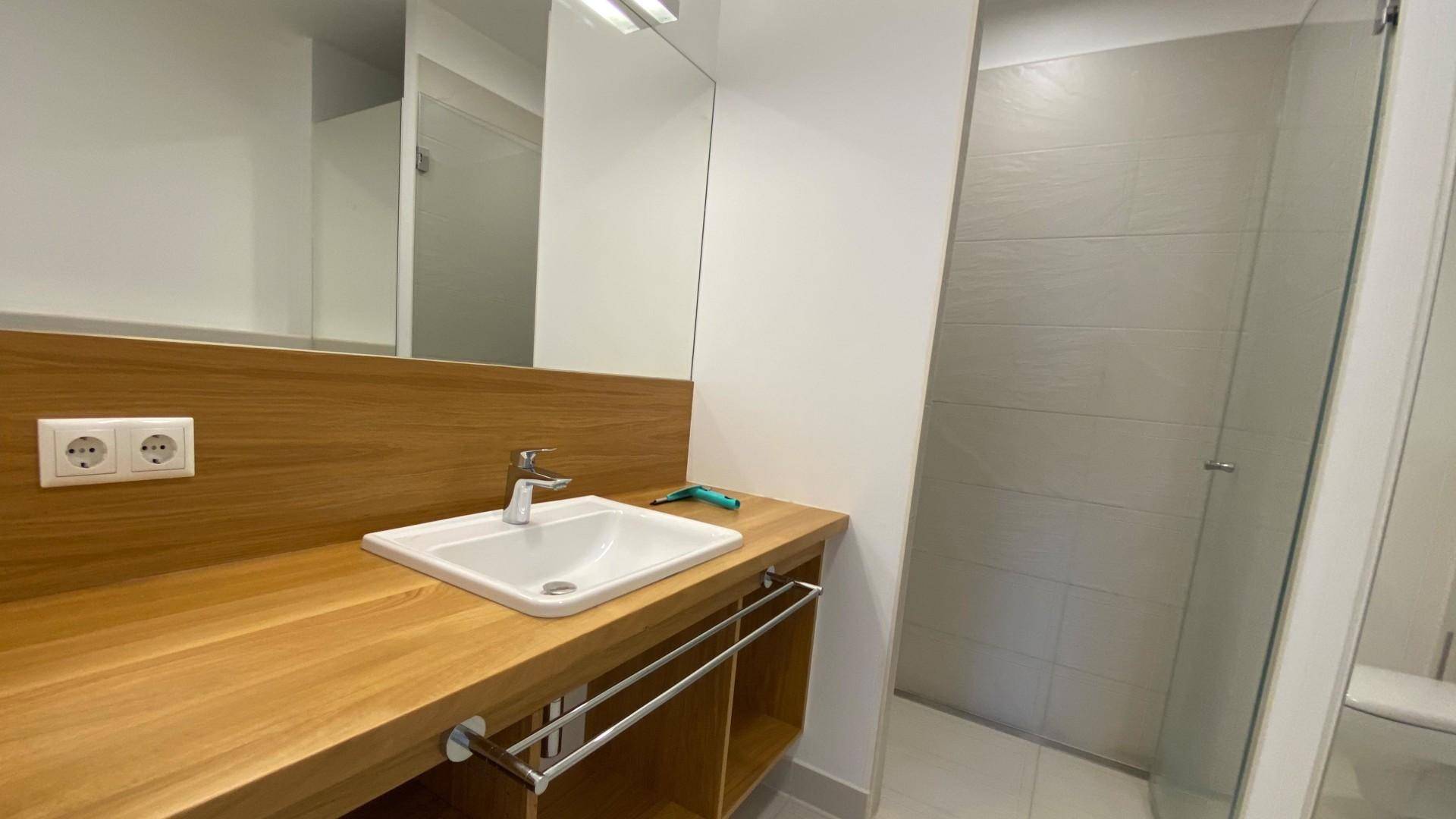 Modernes Badezimmer mit Holzelementen, Einzelwaschbecken und begehbarer Dusche.