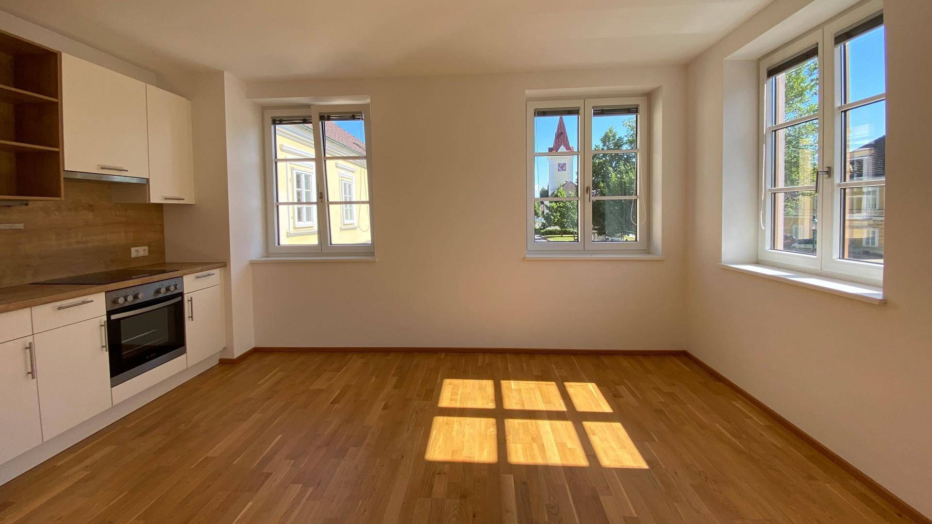 Heller Wohnbereich mit Parkettboden, integrierter Küche und Fenstern mit Blick auf die Umgebung.