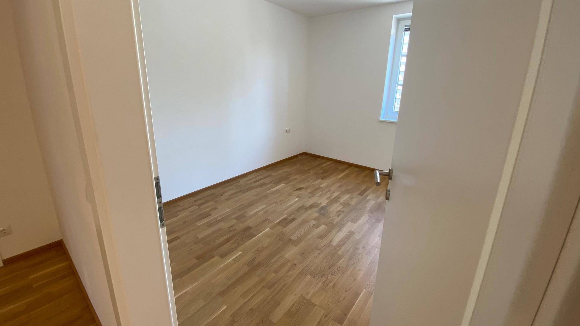 Leeres Schlafzimmer mit hellem Parkettboden und einem Fenster für natürliches Licht.