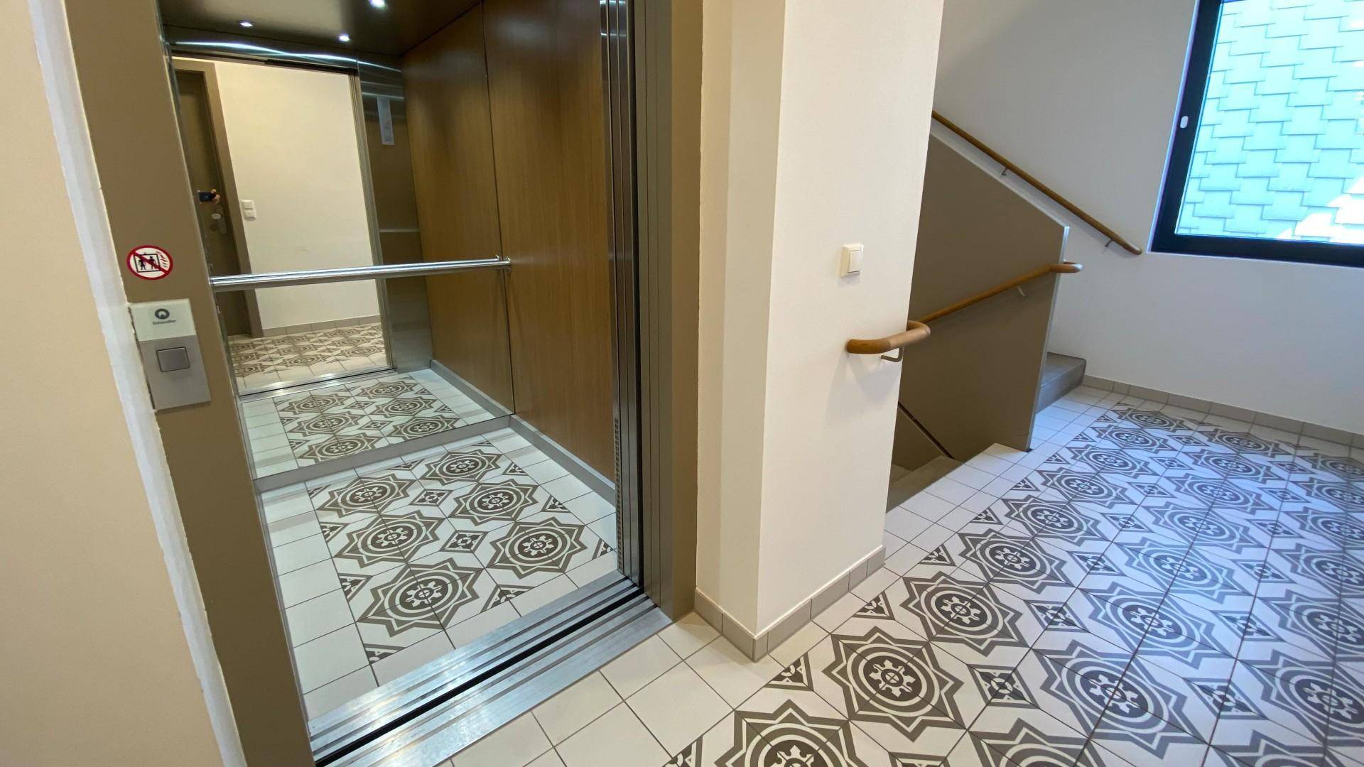 Eingangsbereich mit modernem Aufzug, Treppenhaus und dekorativem Fliesenboden.