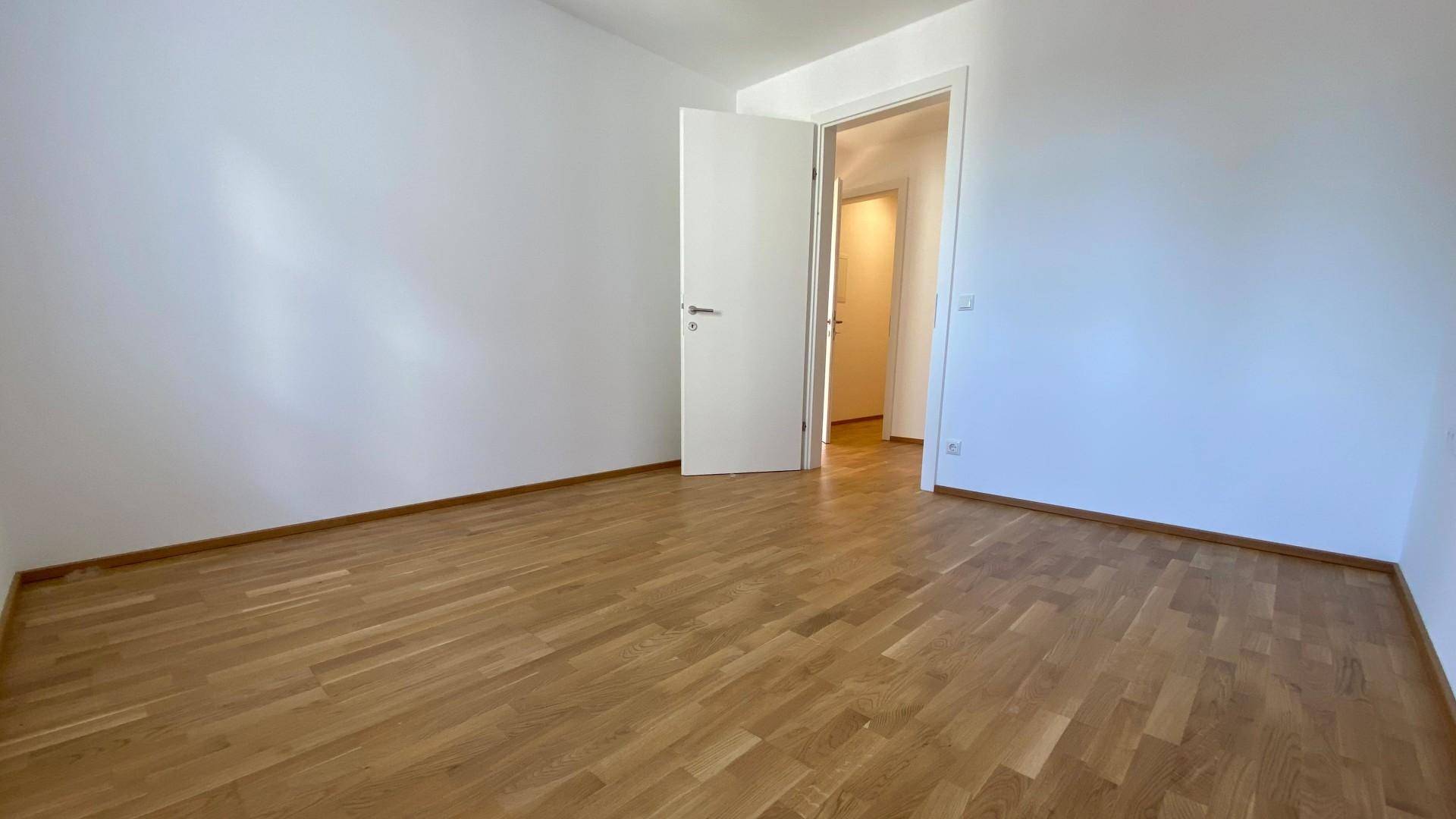 Helles Schlafzimmer mit Parkettboden und weiß gestrichenen Wänden, bereit zur Einrichtung.
