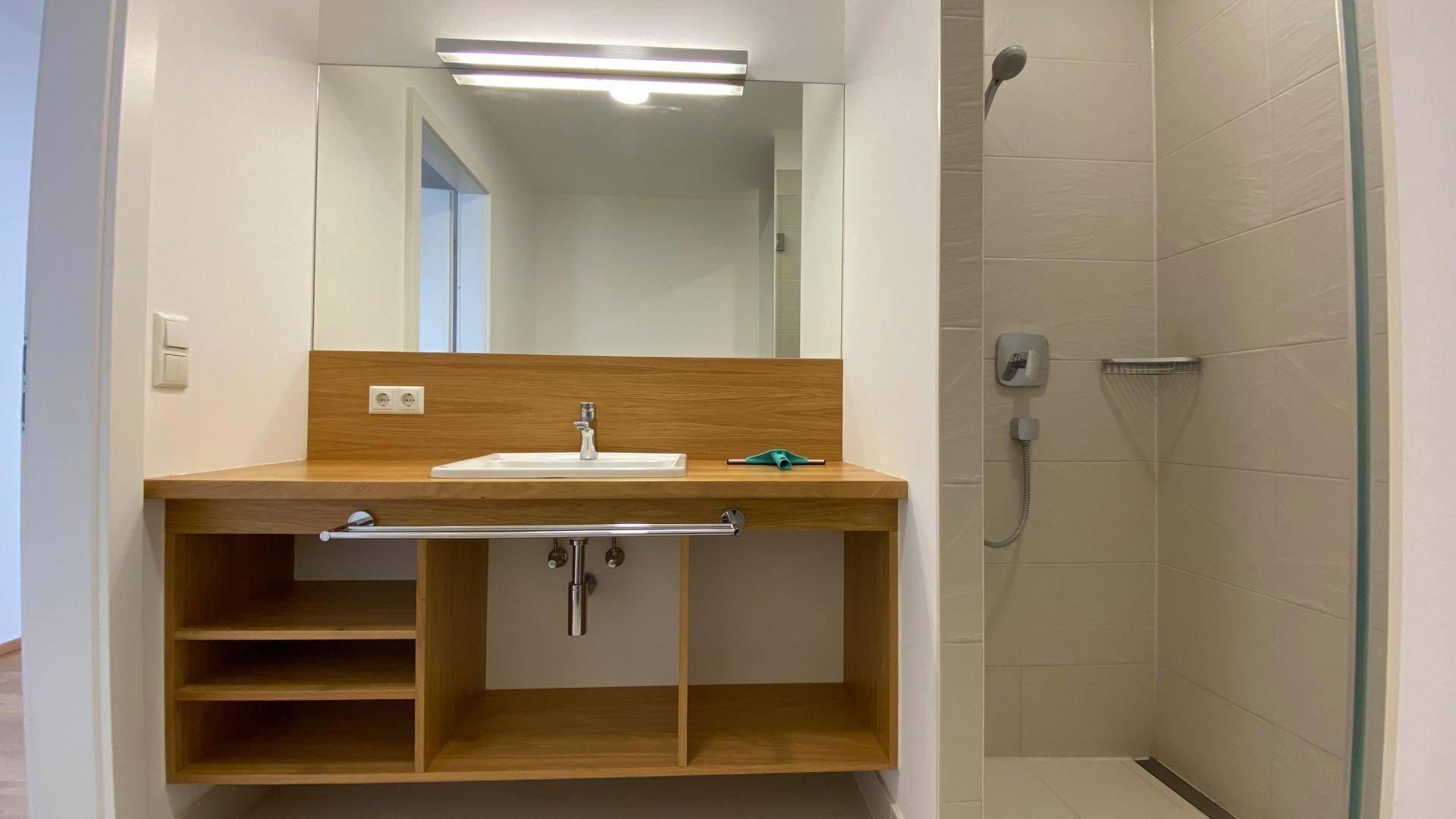 Modernes Badezimmer mit Holzelementen, Einzelwaschbecken und begehbarer Dusche.