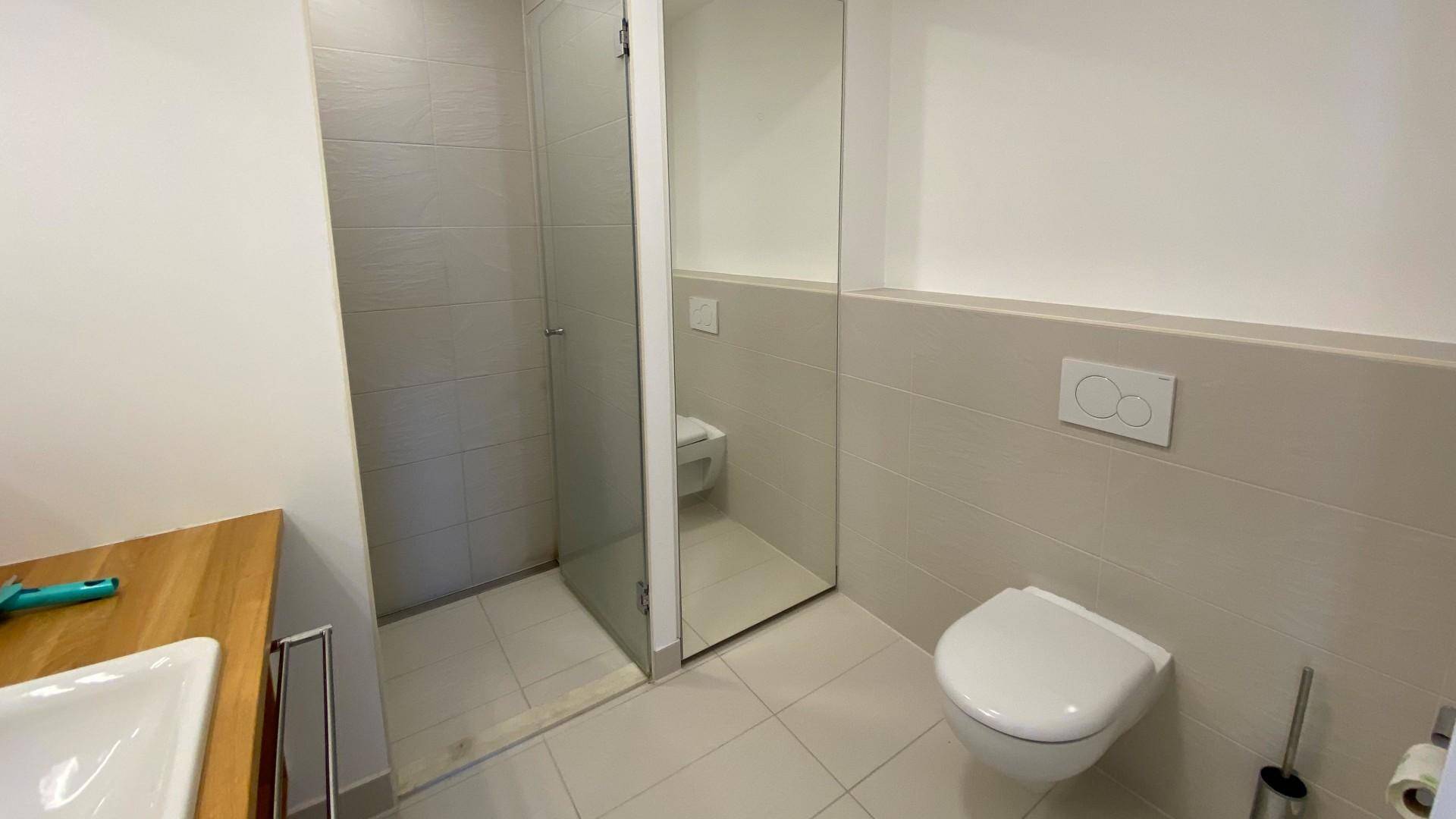 Modernes Badezimmer mit begehbarer Dusche, wandhängendem WC und hellem Fliesenboden.