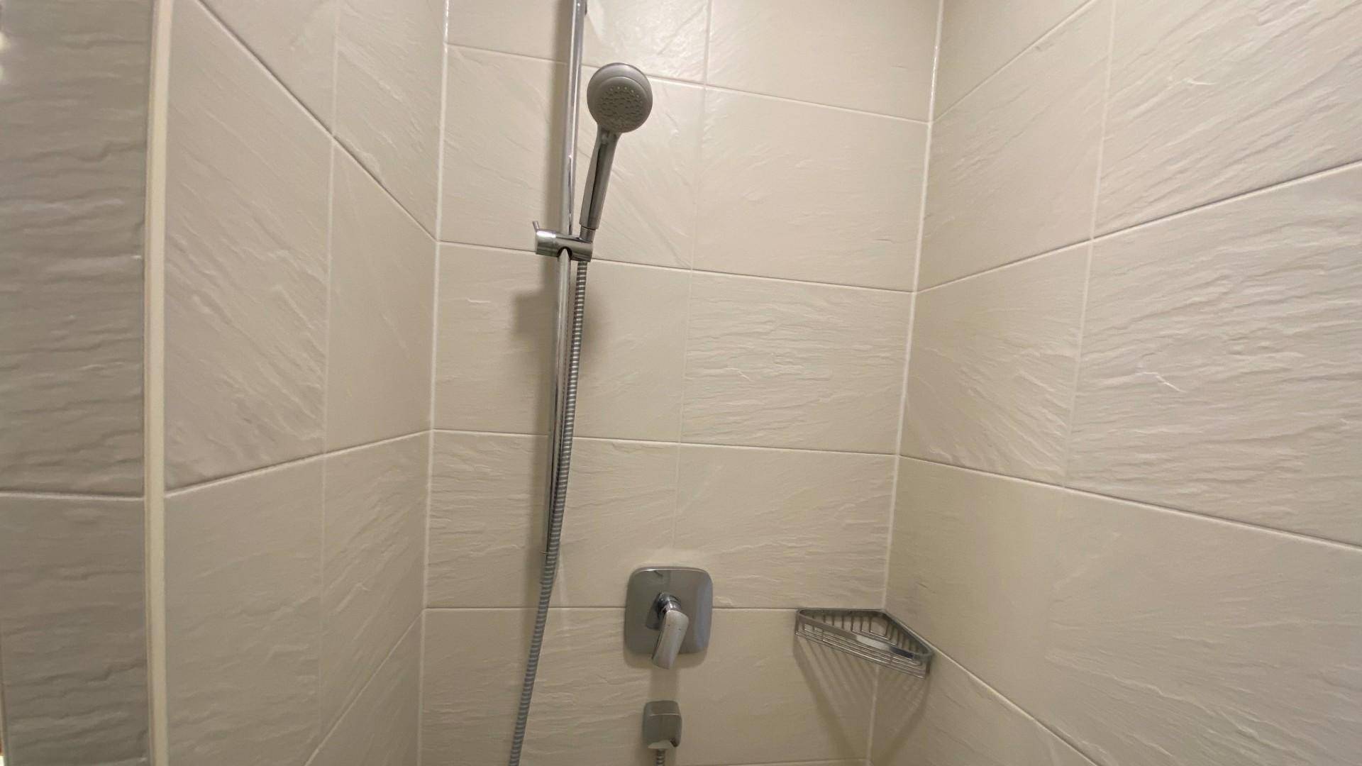 Detailaufnahme einer modernen Duscharmatur und hellen Fliesen in einem Badezimmer.