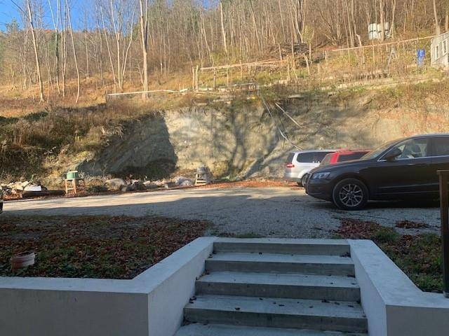 Außenbereich mit Parkplätzen vor einem bewaldeten Hang und einer Treppe zum Gebäude.
