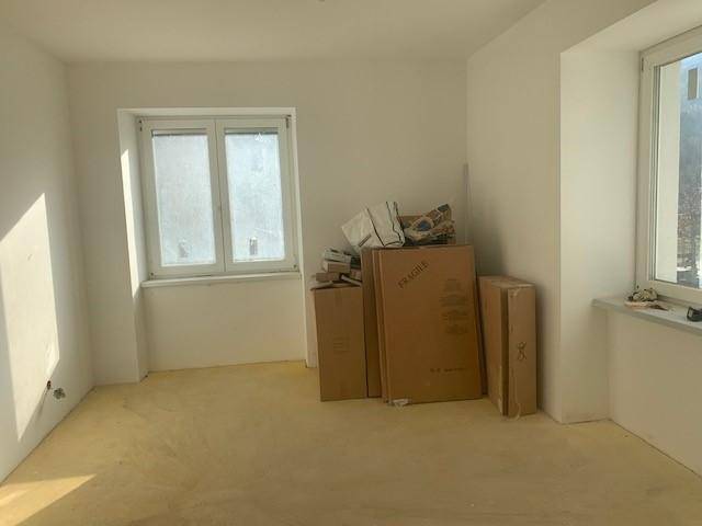 Leeres Zimmer mit zwei Fenstern, weißen Wänden und Kartons, bereit für die Einrichtung.