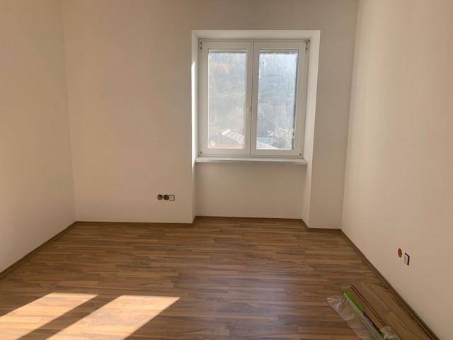 Helles Schlafzimmer mit Laminatboden und einem großen Fenster, das viel Tageslicht hereinlässt.